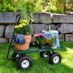 Green Gorilla Made cart with potted plants, gloves, and soil bag on grass.
