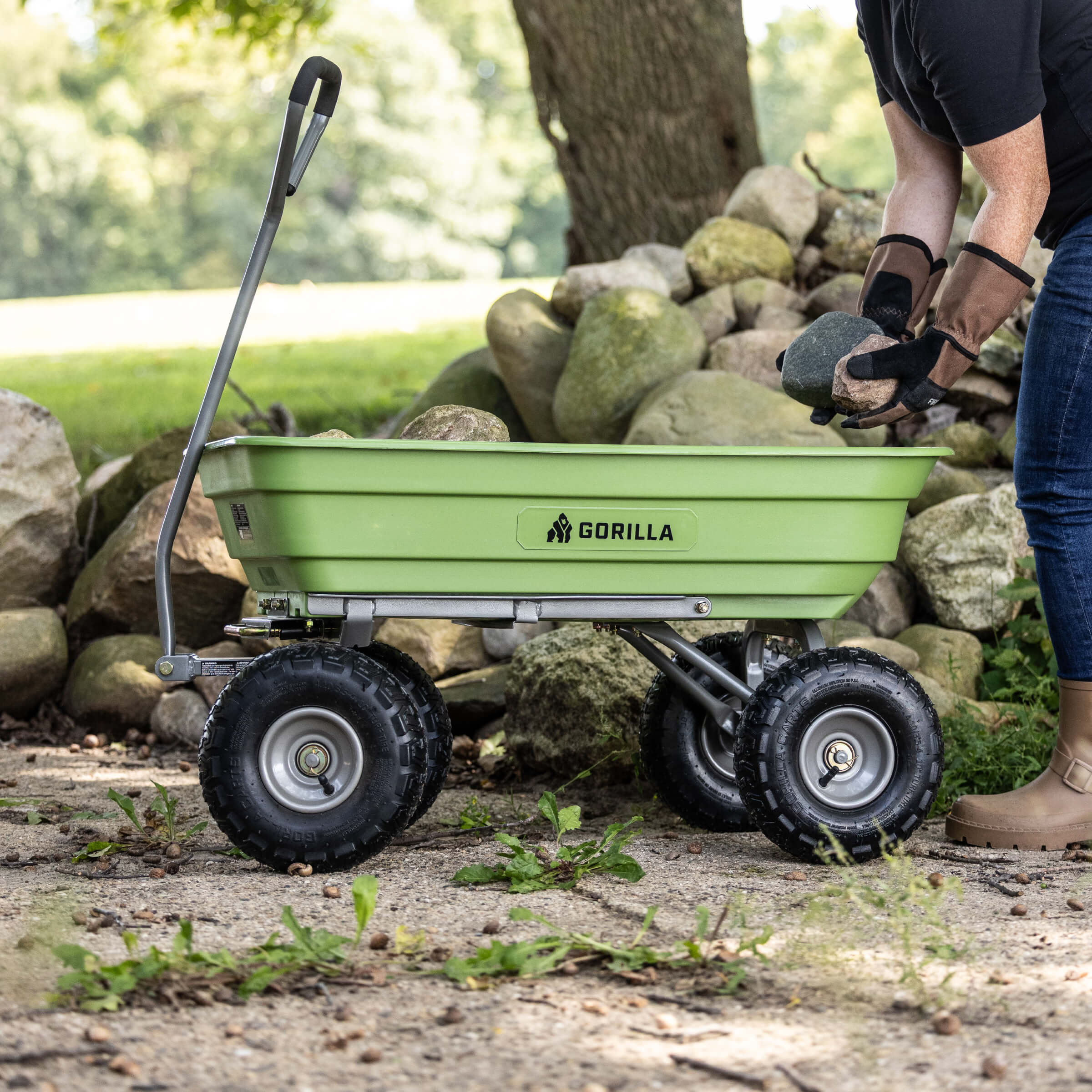 Green Gorilla utility cart with rugged tires on a garden path, person loading rocks.
