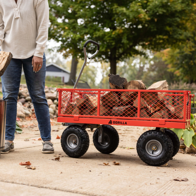 Red Gorilla utility cart filled with firewood on a paved surface outdoors.