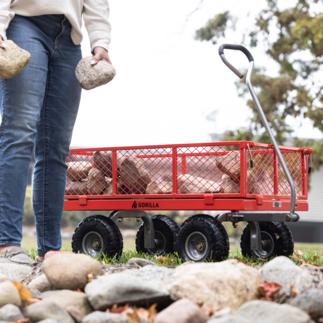Red Gorilla utility cart loaded with stones, person in jeans holding rocks.