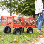 Orange Gorilla utility cart with metal mesh sides carrying firewood on grass.