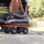 Man loading bags of brown mulch onto an orange Gorilla cart from a truck.