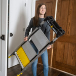 Person holding a Gorilla Ladders folding ladder with gray steps and yellow accents.