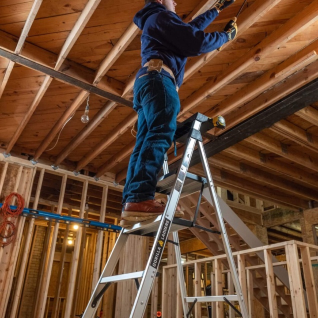 Person using a Gorilla Ladders product in a construction site, holding tools.