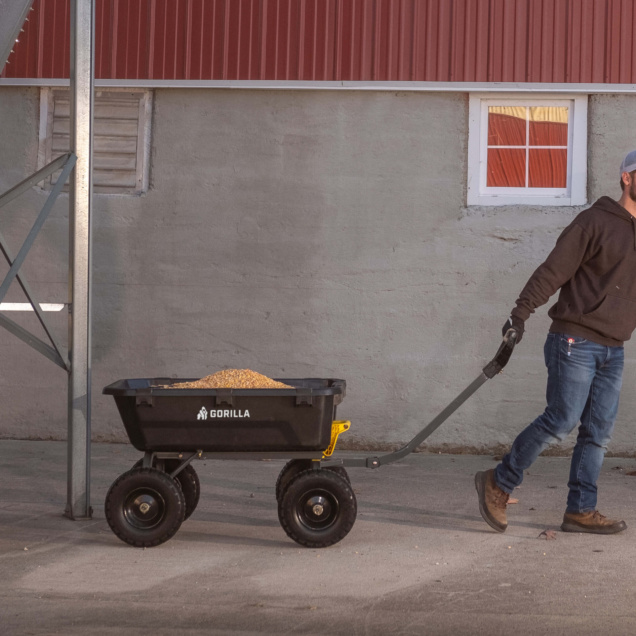 Person pulling a black Gorilla Made utility cart loaded with gravel, against a red and gray building backdrop.