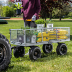 Person with a purple sweater using a Gorilla cart filled with plants and potting mix on grass.