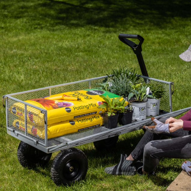 Gorilla Made cart with potting mix and plants on grass, person adjusting glove.