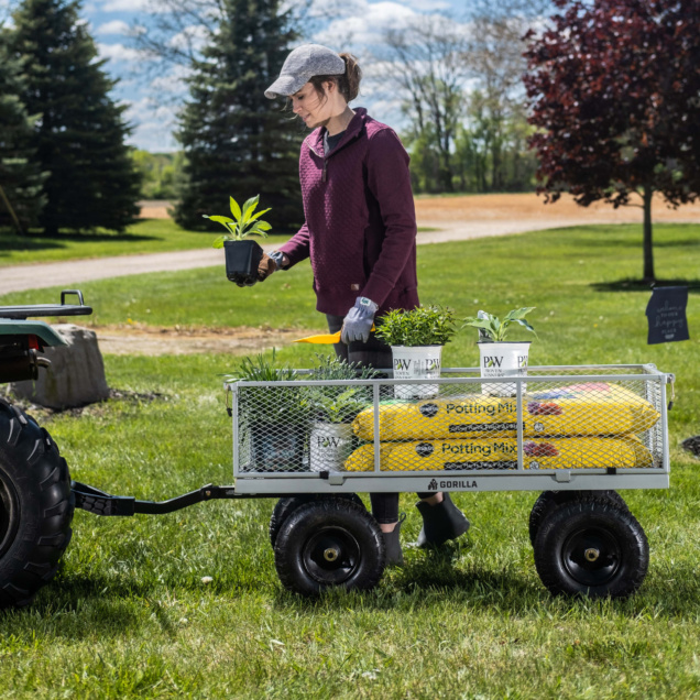 Outdoor scene with a person using a Gorilla Made cart carrying plants and potting mix.