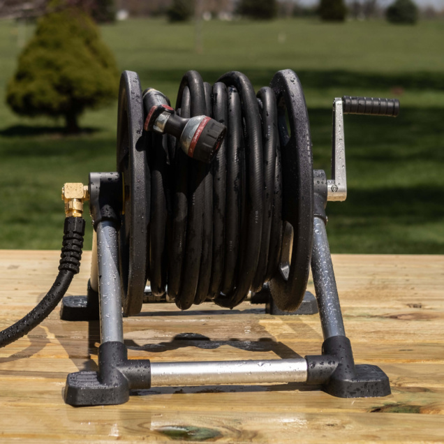 Black garden hose on a metal reel with crank, resting on a wooden surface.