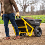 Person moving Gorilla Made black cart with yellow frame filled with soil.