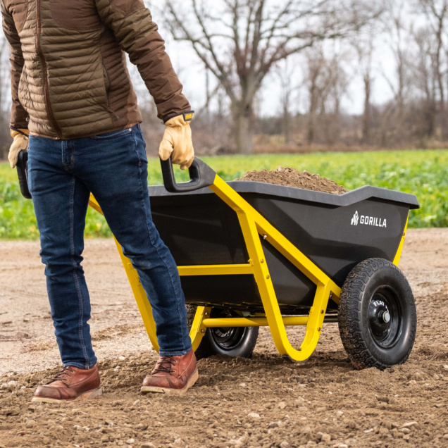 Person moving Gorilla Made black cart with yellow frame filled with soil.