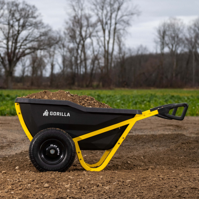 Black and yellow Gorilla wheelbarrow filled with soil on a dirt path.