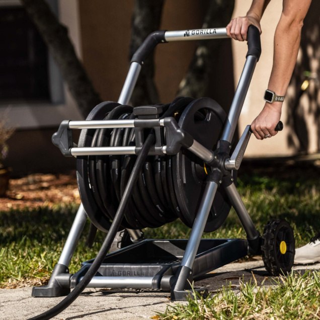 Person using a silver Gorilla hose reel on a sunny day.