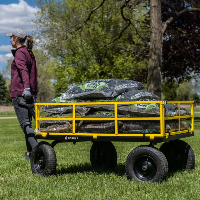 Person pulling a yellow Gorilla Made utility cart loaded with garden supplies.