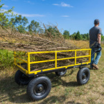 Yellow Gorilla Made cart carrying branches in a field with a person pulling it.