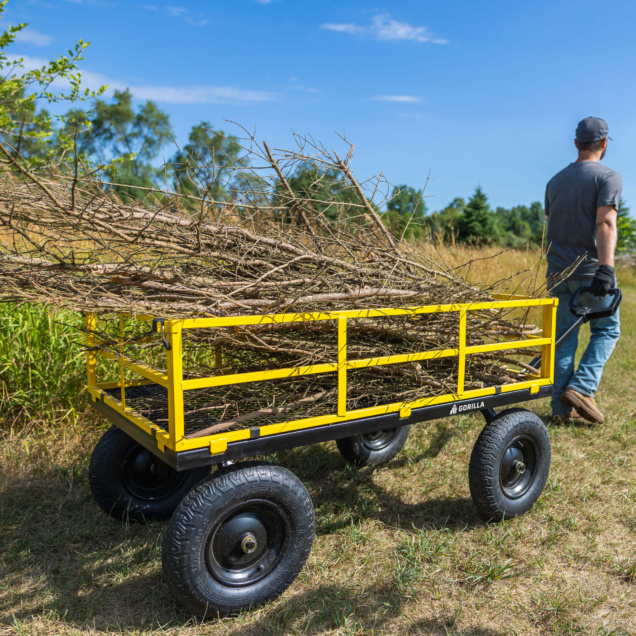Yellow Gorilla Made cart carrying branches in a field with a person pulling it.