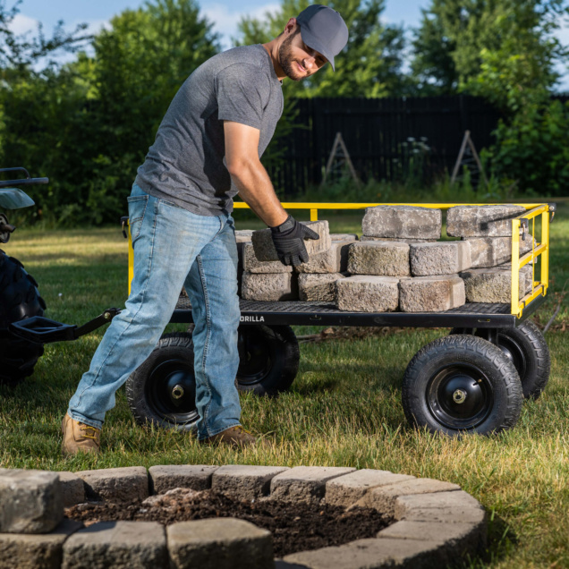 Person uses Gorilla Made's utility cart with yellow frame to transport gray bricks.