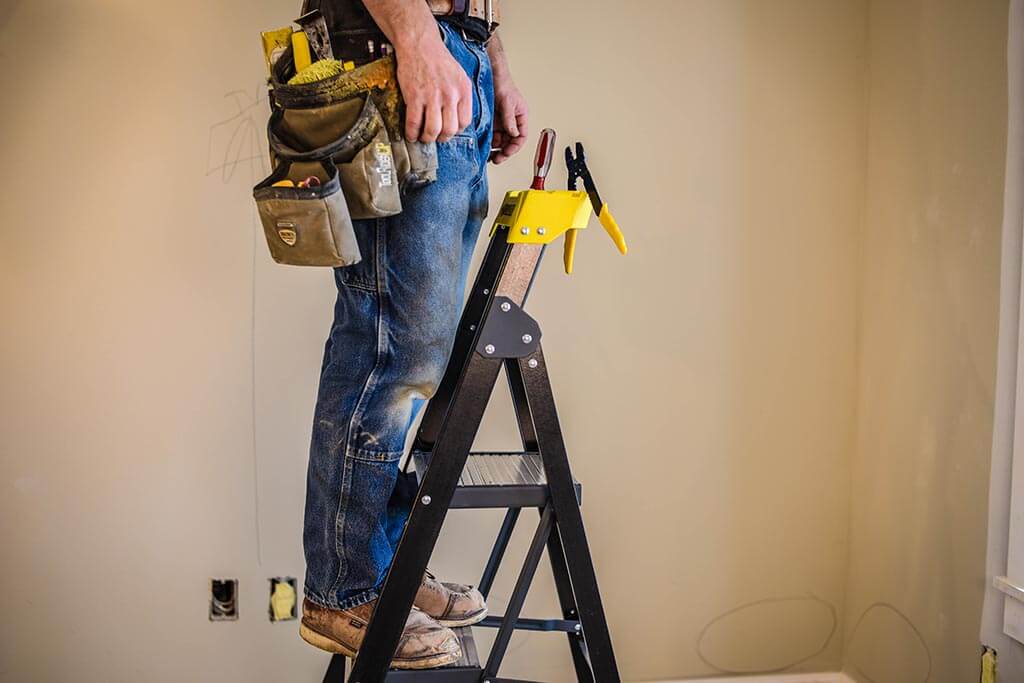 Person standing on a black Gorilla Made ladder with tools in a belt.