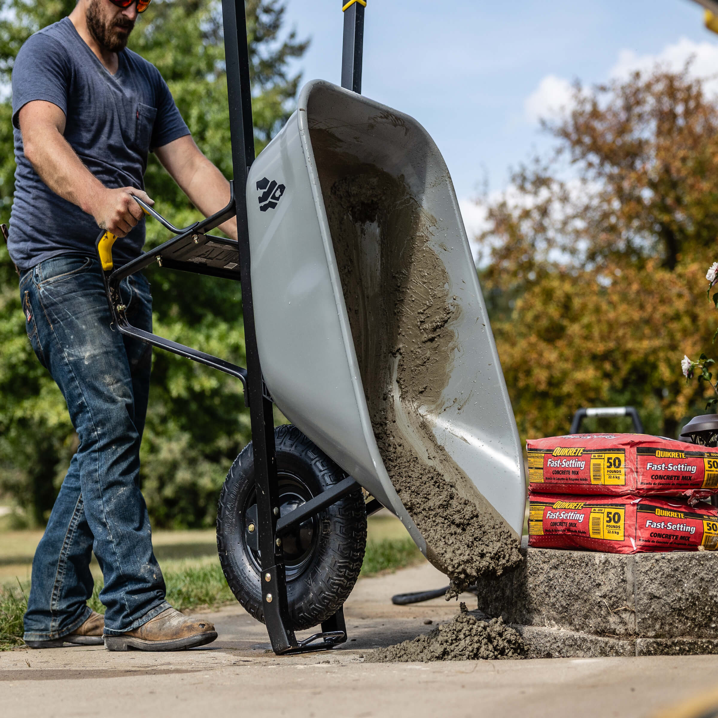 Person using Gorilla Made gray wheelbarrow to pour concrete beside "Quikrete Fast-Setting."