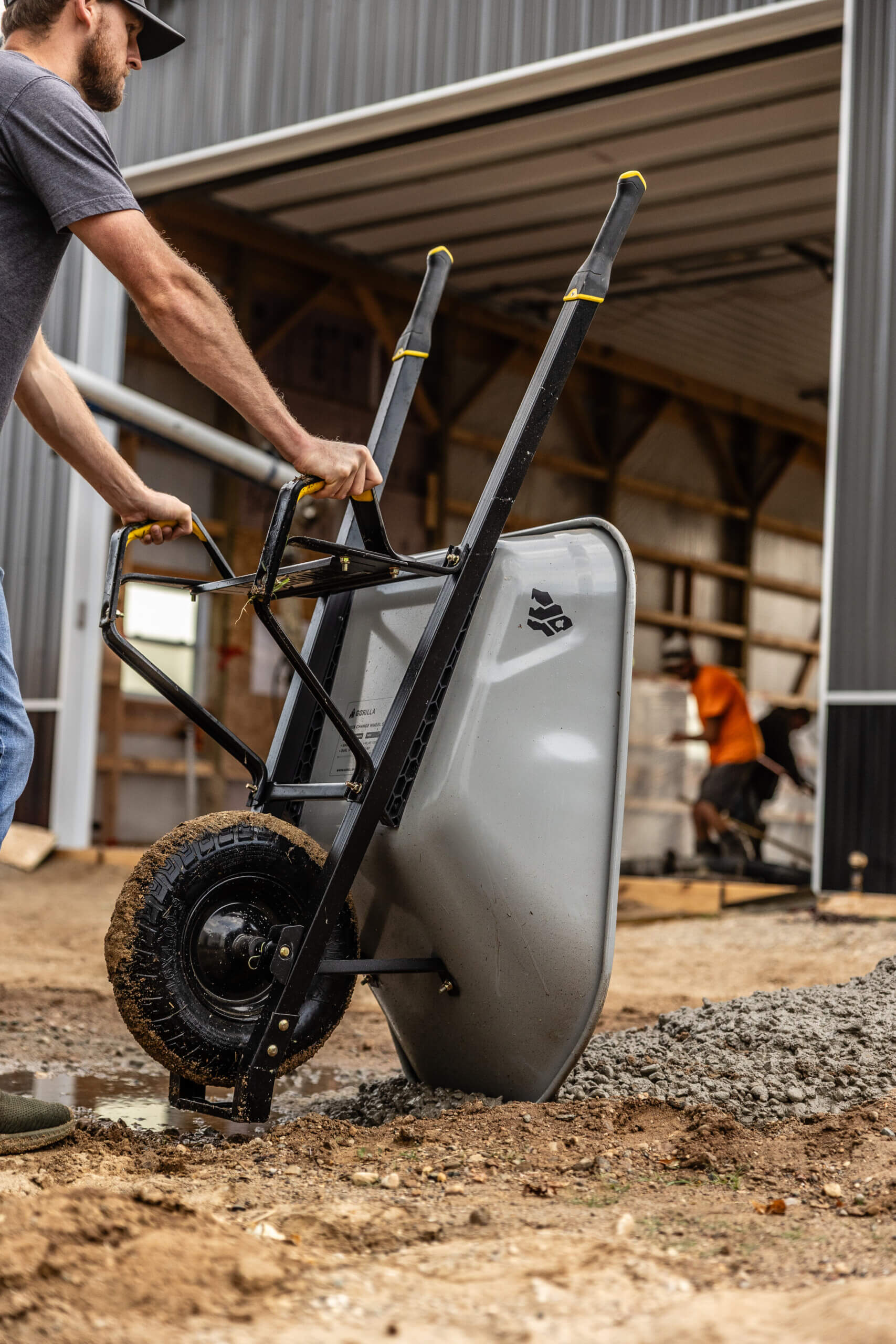 A person using a Gorilla Made GSXD wheelbarrow, gray with black handles, in a construction site.