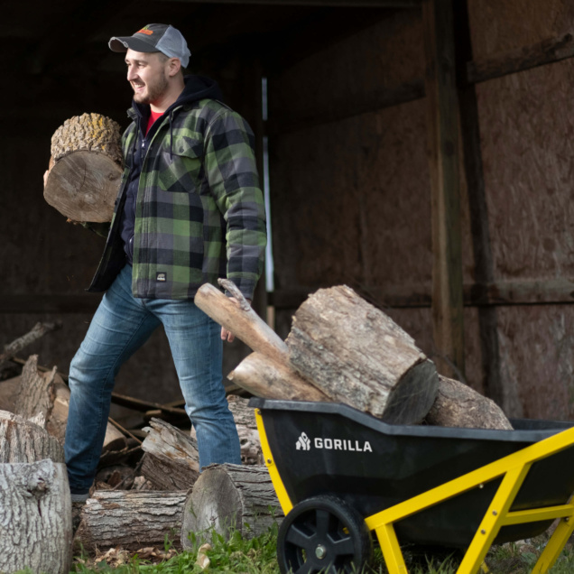 Person in plaid jacket moves logs with a yellow and black Gorilla cart.