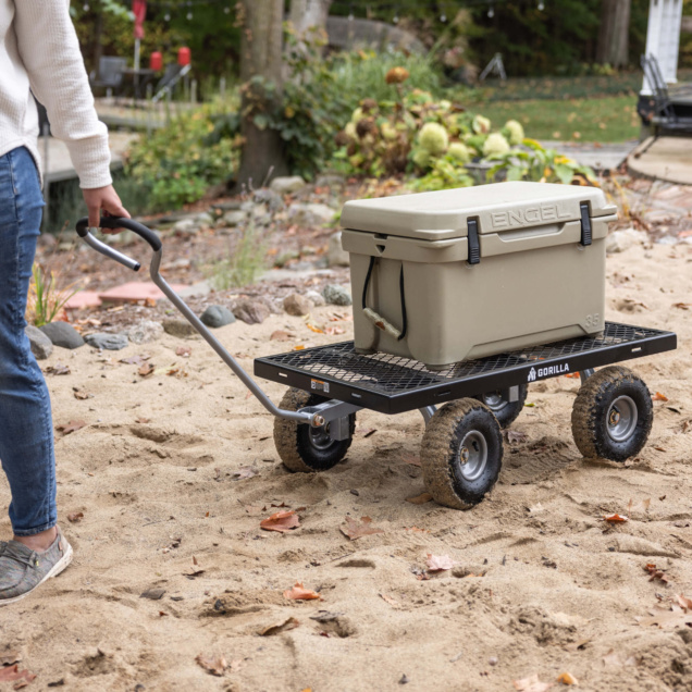 A person pulls a black Gorilla cart on sand, carrying a beige cooler labeled "ENGEL."