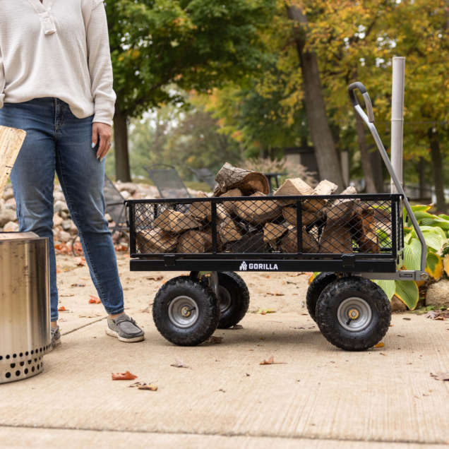 Gorilla utility cart with firewood, black mesh sides, and logo on a concrete path.
