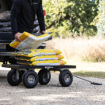 Gorilla cart with four wheels, loaded with yellow bags, near a truck.
