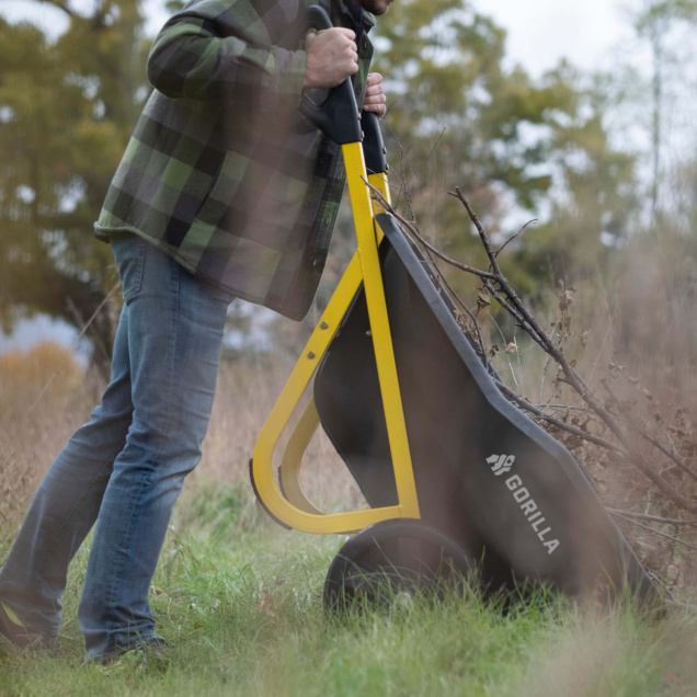 Person using a Gorilla Made utility cart with branches, yellow handles, outdoors.