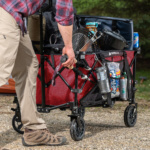 Red Gorilla utility cart loaded with outdoor gear and beverages, wheels on gravel.
