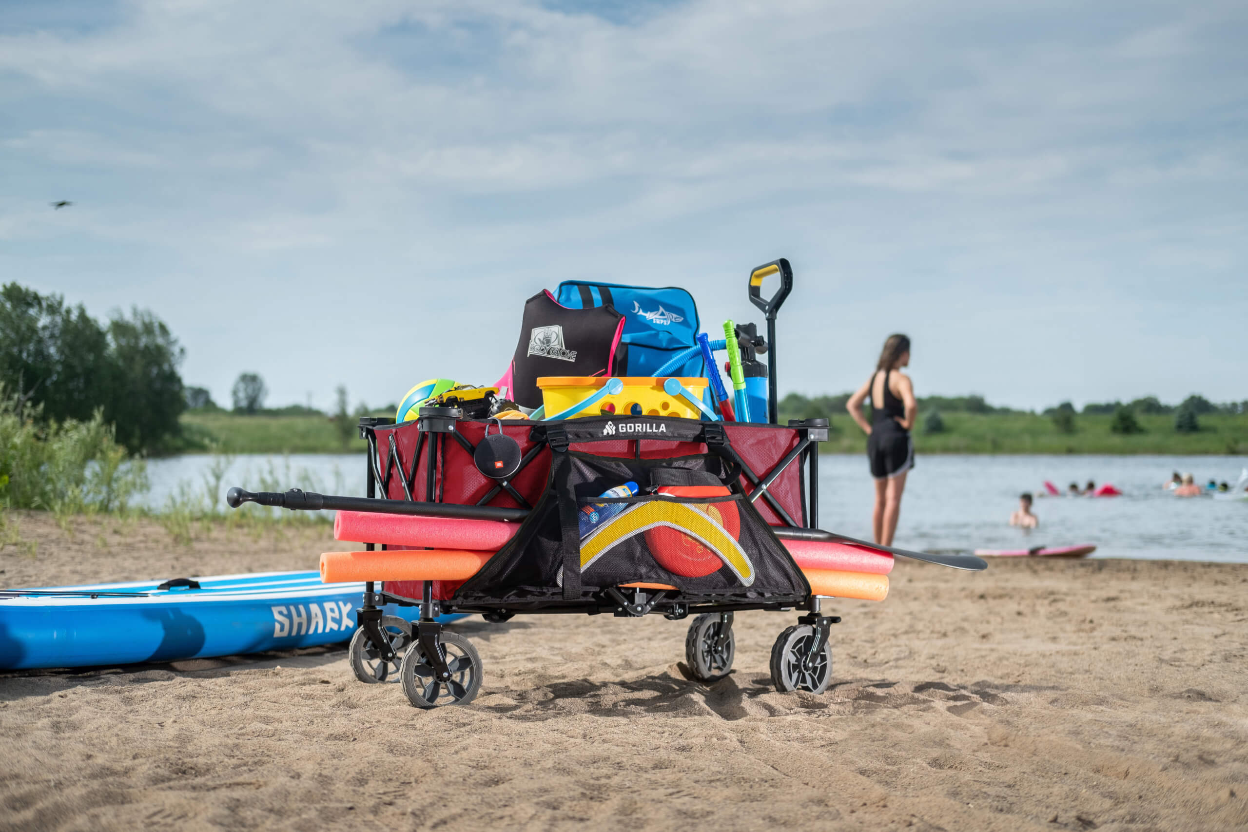 Red Gorilla cart loaded with beach gear on sandy shore near a lake.