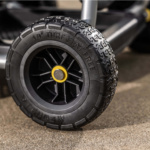 Close-up of a black 10" Turf Flat Free tire with a yellow hub on a gray utility cart.