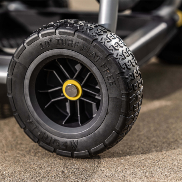 Close-up of a black 10" Turf Flat Free tire with a yellow hub on a gray utility cart.