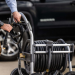 Silver and black hose reel cart in use next to a dark vehicle.