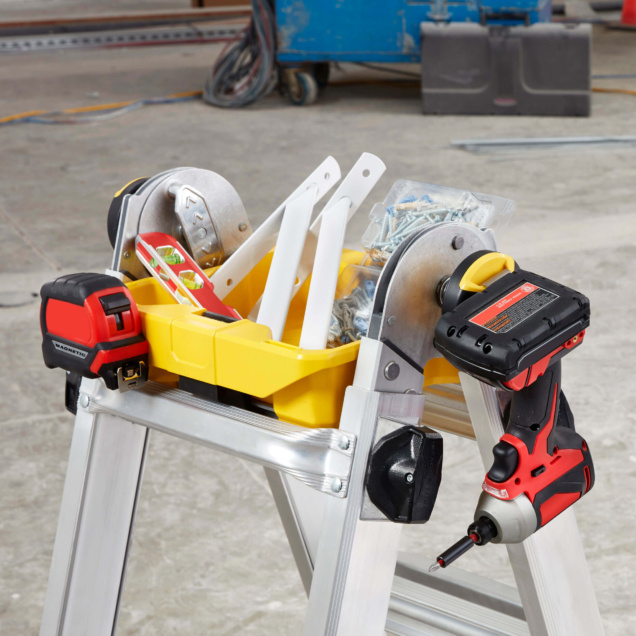 Silver Tricam ladder with yellow tool tray holding tools and screws, in a workshop setting.
