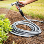 Hand holding a Gorilla Made garden hose with water spraying on greenery.