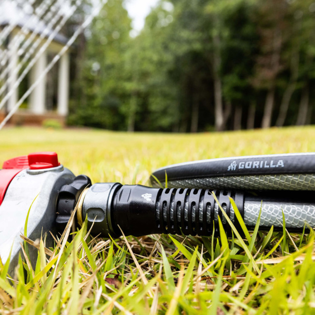 Close-up of Gorilla-branded hose with nozzle, lying on green grass in a garden.