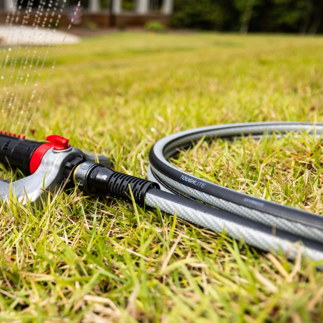 Grey garden hose labeled "ToughLite" on grass, attached to a red and black nozzle.