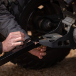 Black 2-in-1 towable handle being attached to a vehicle by hand.