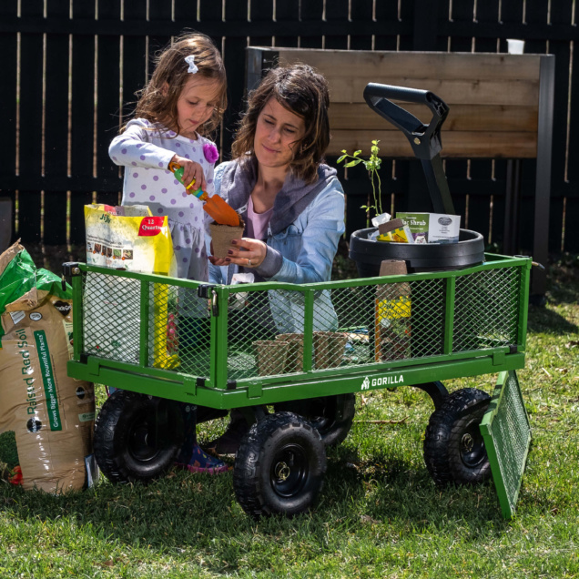 Green Gorilla cart with gardening supplies and two people planting in pots.