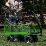 Person placing branches in green Gorilla-made utility wagon in grassy area.