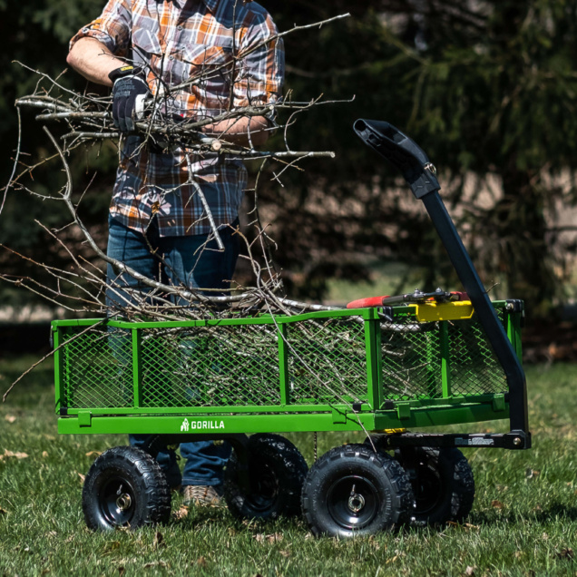 Person placing branches in green Gorilla-made utility wagon in grassy area.
