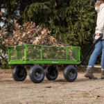Green Gorilla Made utility cart carrying branches, pulled on a dirt path.