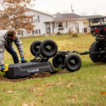 Person adjusts black Gorilla utility cart attached to ATV on grassy field.