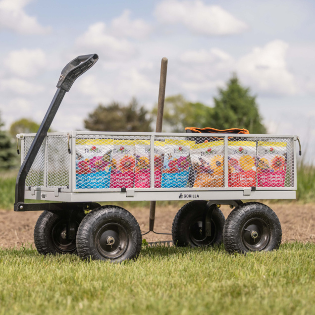 Gorilla Made utility cart loaded with colorful Burpee soil bags on grassy terrain.