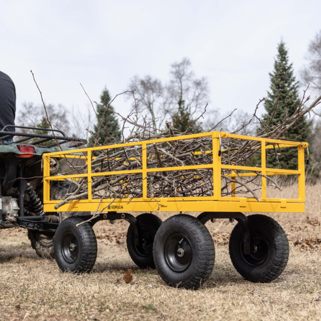 Yellow Gorilla Made utility cart loaded with branches, pulled by a vehicle.
