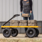 A person lifts bricks onto a yellow Gorilla utility cart with large black wheels.