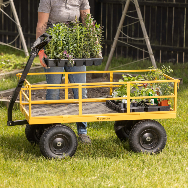 Person moving plants with a yellow Gorilla utility cart on grassy lawn.