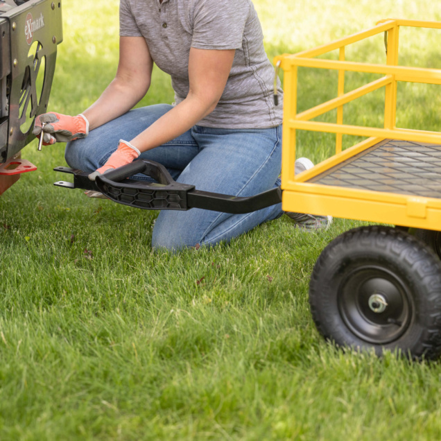 Person connecting yellow Gorilla Made utility cart to exmark machine in grassy area.