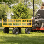 Yellow Gorilla utility cart with black wheels hitched to a lawn mower on grass.